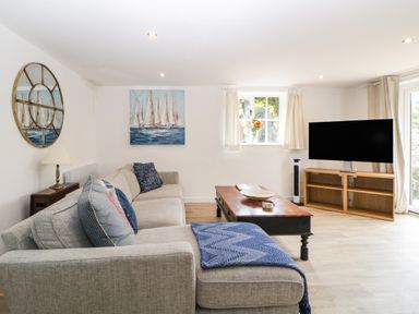 A living room with a beige sofa a wooden coffee table a flat screen tv and a window with curtains at The Holt in Harcombe near Sidford