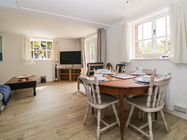A dining area with a wooden table set for four and a living room with a television and coffee table at The Holt in Harcombe near Sidford