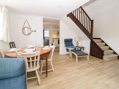 A dining area with a round wooden table set for four and a blue armchair with footstool near stairs at The Holt in Harcombe near Sidford
