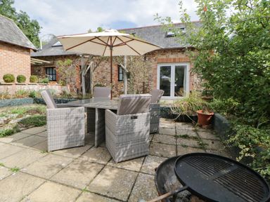 An outdoor patio with a dining table set under an umbrella and a barbecue grill at The Holt in Harcombe near Sidford