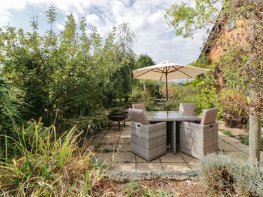 A garden patio with a table and four chairs under an umbrella surrounded by plants and trees at The Holt in Harcombe near Sidford