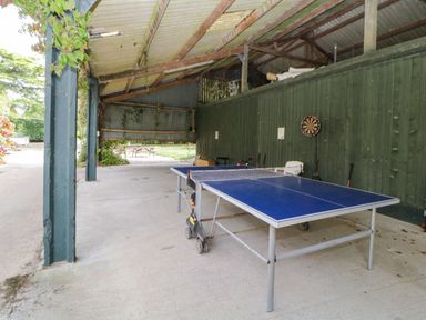 A covered outdoor area with a ping pong table and a dartboard on a green wall at The Holt in Harcombe near Sidford