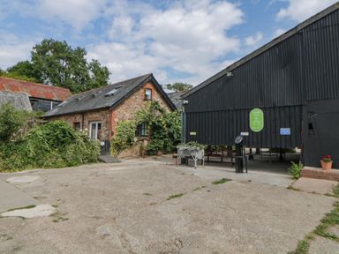 A courtyard with a stone building covered in ivy and a black barn with an open entrance at The Holt in Harcombe near Sidford
