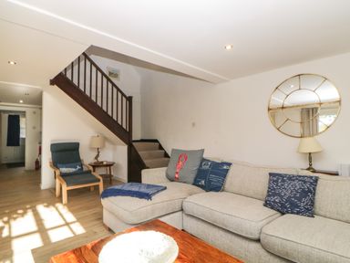 A living room with a beige sofa and blue cushions a wooden staircase a blue armchair and a round mirror on the wall at The Holt in Harcombe near Sidford