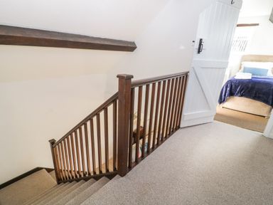 A staircase with wooden banister leading to a bedroom with a bed covered by a blue blanket at The Holt in Harcombe near Sidford