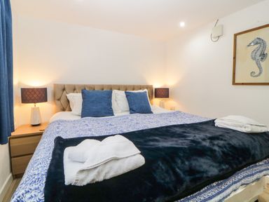 A bedroom with a bed with blue and white bedding two blue pillows two lamps on wooden nightstands and a seahorse picture on the wall at The Holt in Harcombe near Sidford