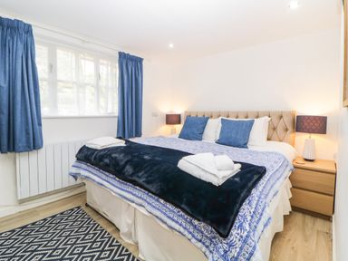 A bedroom with a bed covered with blue and white bedding two blue pillows and a black throw blanket two bedside tables with lamps and blue curtains on the window at The Holt in Harcombe near Sidford