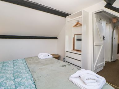 A bedroom with a bed covered by a green blanket and white towels on top a white open wardrobe with wooden hangers and a mirror and a hallway with white doors