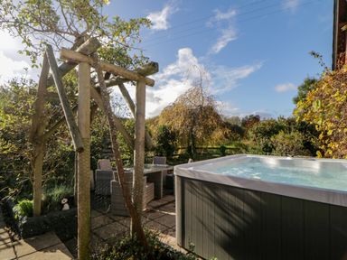An outdoor patio with a hot tub a glass table with chairs and wooden garden supports at The Holt in Harcombe near Sidford