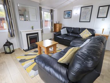A living room with black leather sofas a wooden coffee table a fireplace and framed pictures on the wall at Lavender Lodge in Applethwaite 4 Limefitt Park near Windermere