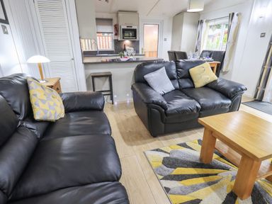 A living room with black leather sofas and a wooden coffee table next to a kitchen area at Lavender Lodge in Applethwaite 4 Limefitt Park near Windermere