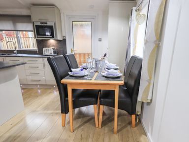 A dining area with a wooden table set for four with black chairs next to a kitchen counter at Lavender Lodge in Applethwaite 4 Limefitt Park near Windermere