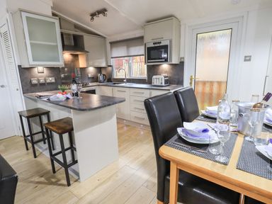 A kitchen with bar stools an oven microwave and dining table set with plates glasses and napkins at Lavender Lodge in Applethwaite 4 Limefitt Park near Windermere