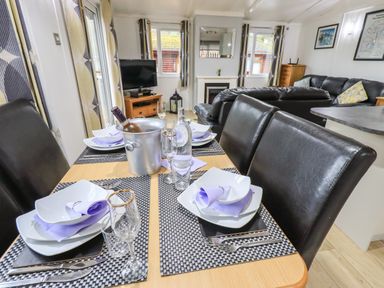 A dining table set with plates napkins glasses and a wine bucket in a living room with sofas and a television at Lavender Lodge Applethwaite 4 Limefitt Park near Windermere