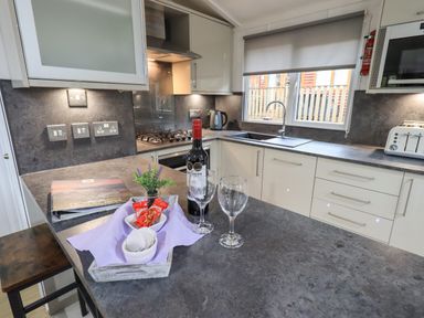 A kitchen with a countertop holding a bottle of wine two wine glasses snacks a small plant a sink a window and various appliances at Lavender Lodge Applethwaite 4 Limefitt Park near Windermere