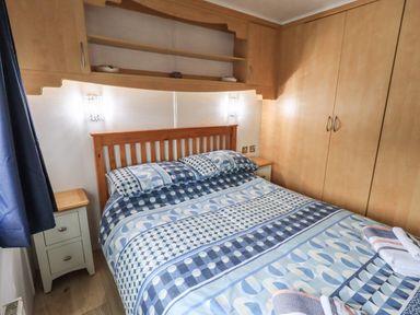 A bedroom with a bed and patterned bedding wooden headboard bedside tables and built in wooden storage at Lavender Lodge Applethwaite 4 Limefitt Park near Windermere