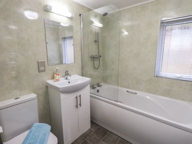 A bathroom with a toilet a sink with cabinet a bathtub with shower and a window at Lavender Lodge Applethwaite 4 Limefitt Park near Windermere