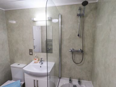 A bathroom with a toilet sink with soap mirror light and a shower over a bathtub at Lavender Lodge Applethwaite 4 Limefitt Park near Windermere