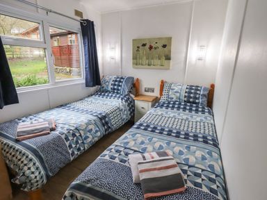 A bedroom with two single beds with patterned bedding and a window showing an exterior view at Lavender Lodge Applethwaite 4 Limefitt Park near Windermere