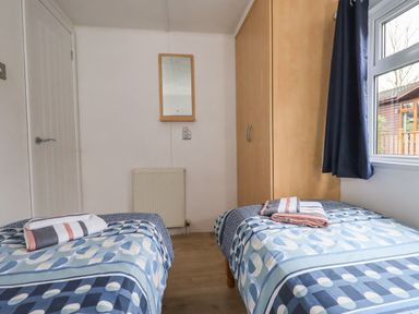 A small bedroom with two single beds with geometric patterned bedding and folded towels at Lavender Lodge Applethwaite 4 Limefitt Park near Windermere