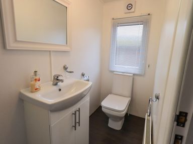 A bathroom with a sink and cabinet a mirror a toilet a window with blinds and a radiator at Lavender Lodge Applethwaite 4 Limefitt Park near Windermere