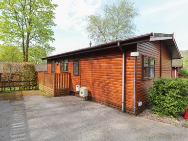 A wooden cabin with a small porch and fenced yard surrounded by trees at Lavender Lodge in Applethwaite 4 Limefitt Park near Windermere