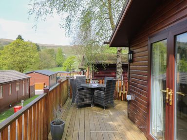 A wooden balcony with a table and four chairs overlooking trees and nearby cabins at Lavender Lodge Applethwaite 4 Limefitt Park near Windermere
