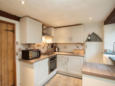 A kitchen with cabinets microwave oven kettle bread box and wine bottle at Rustic Cottage in Bowness-On-Windermere