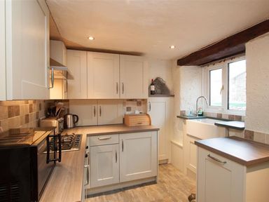 A kitchen with white cabinets a microwave kettle stove and a window at Rustic Cottage in Bowness-On-Windermere