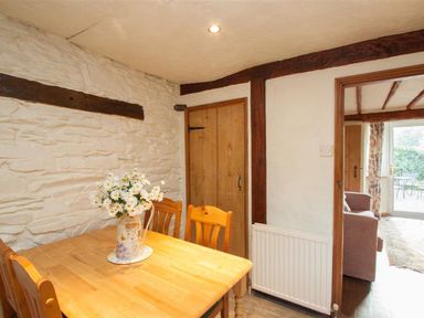 A dining area with a wooden table and chairs a vase with flowers on the table and a door leading to a living room at Rustic Cottage in Bowness-On-Windermere