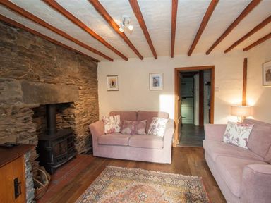 A living room with two pink sofas a stone fireplace a rug and exposed wooden beams at Rustic Cottage in Bowness-On-Windermere