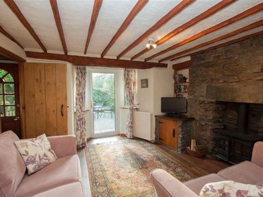 A living room with a fireplace two sofas a rug and a door leading outside at Rustic Cottage in Bowness-On-Windermere