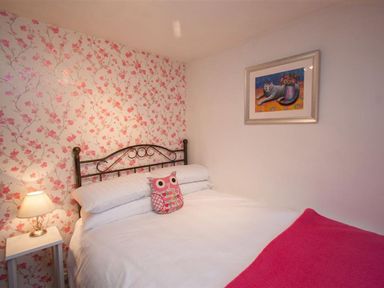 A bedroom with a double bed pink floral wallpaper and a painting of a cat at Rustic Cottage in Bowness-On-Windermere
