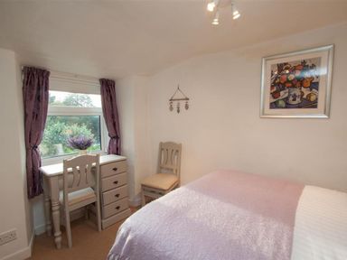 A bedroom with a bed a desk two chairs and a window with purple curtains at Rustic Cottage in Bowness-On-Windermere