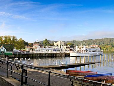A lakeside pier with boats docked and swans in the water at Rustic Cottage in Bowness-On-Windermere