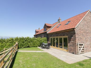 An outdoor patio area with a table and chairs next to a brick house with large windows at Kaitkyella Lodge in Scarborough