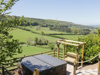 An outdoor patio with a covered hot tub and wooden swing overlooking green fields and hills at Kaitkyella Lodge in Scarborough