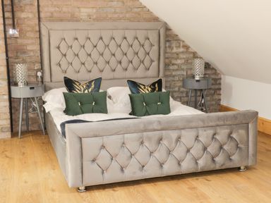 A bedroom with a gray upholstered bed and two bedside tables with lamps at Kaitkyella Lodge in Scarborough