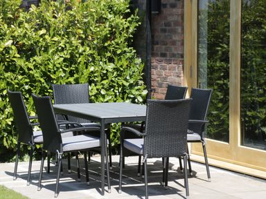 A patio area with a rectangular table and six wicker chairs near glass doors and greenery at Kaitkyella Lodge in Scarborough