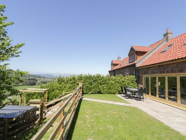 A garden with patio furniture next to a brick house with red roof tiles at Kaitkyella Lodge in Scarborough