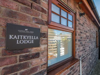 A brick exterior wall with a wooden framed window and a sign reading Kaitkyella Lodge at Stepney Hill Farm in Scarborough