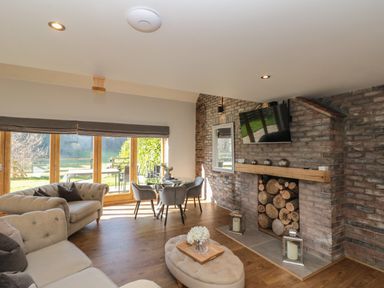A living room with large glass doors a table with chairs a fireplace with stacked logs and a mounted tv at Kaitkyella Lodge in Scarborough