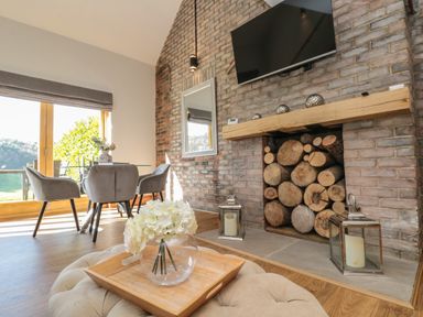 A living room with a fireplace filled with logs a glass dining table with chairs and a flower vase at Kaitkyella Lodge in Scarborough