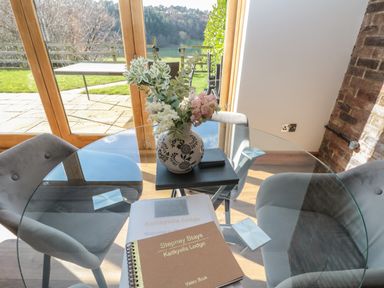 A glass dining table with a vase of flowers and a visitor book on it in a room with grey chairs at Kaitkyella Lodge in Scarborough