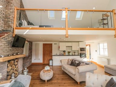 A living room with a sofa ottoman wooden floor and a kitchen with white cabinets at Kaitkyella Lodge Scarborough