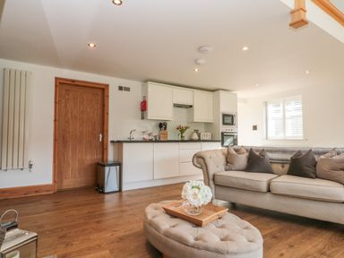A living room with a beige sofa and ottoman in front of a kitchen with white cabinets at Kaitkyella Lodge in Scarborough