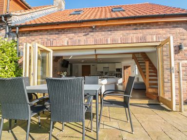 An outdoor patio with a table and six chairs leading to an open indoor living space with a staircase and kitchen at Kaitkyella Lodge in Scarborough