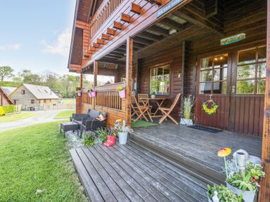 A wooden porch with chairs tables flower pots and a wreath on the door at Sun View Lodge in Llanbedr