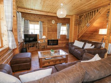 A living room with brown sofas a wooden coffee table a television and wooden walls at Sun View Lodge in Llanbedr