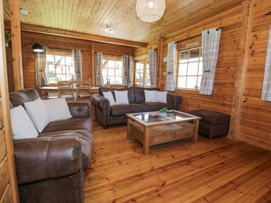 A wooden living room with two brown sofas white pillows a wooden coffee table and windows with plaid curtains at Sun View Lodge in Llanbedr